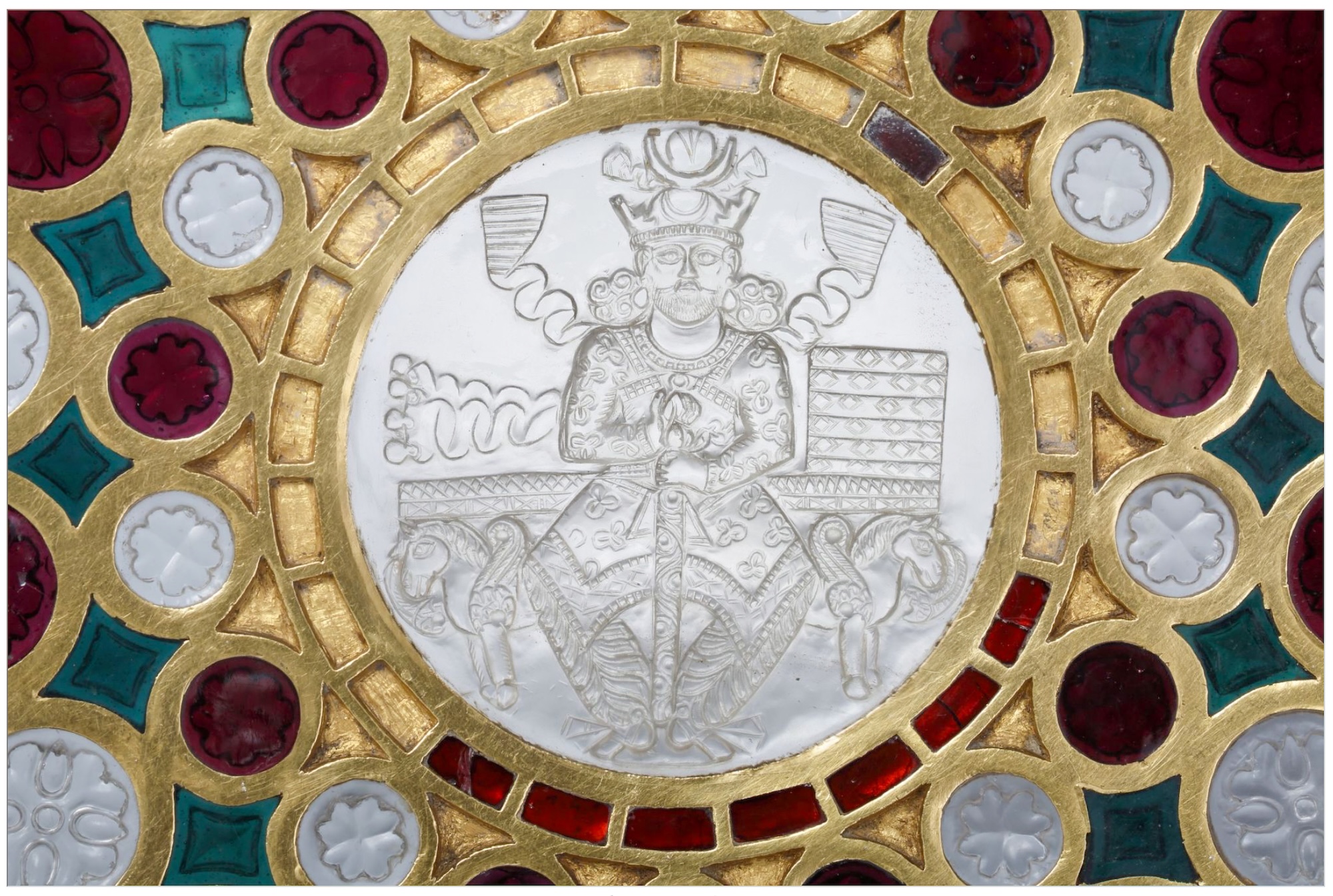 Sassanid Cup (Cup of Solomon), Iran, 6th century CE, rock crystal cameo, gold, garnet, and green glass, H. 5 cm, D. 28.2 cm, Bibliothèque nationale de France, Département des Monnaies, Médailles et Antiques, Cameo.379. The central medallion, engraved in cameo on the reverse of a disc of exceptional rock crystal, depicts a Sassanid king enthroned on a banquet bed whose feet are formed by protomes of winged horses. Dressed in embroidered court costume and wearing a pendant necklace and pear earrings, the king bears a crenellated crown adorned with a crescent moon on the forehead and surmounted by a second crescent enclosing the korymbos — the solar globe of Sassanid royal iconography. The smooth, uncurled beard is specific to Kavadh I (r. 488–531), who is the most plausible candidate for the cup's patron. Kavadh I's successor after his second reign was Khosrow I, whose wars againts Emperor Justinian are documented by al-Ṭabarī. The six cushions of the banquet bed, with the bed itself forming the seventh, symbolise the seven kešvars or climates over which the Sassanid king reigned as master of the world. The medallion is set within a heavy gold mesh enclosing three concentric rows of rock crystal roundels and Rajasthani almandine garnets alternating with deep green glass lozenges, all carved in relief with florets on their reverse. A Pahlavi inscription engraved on the interior of the foot records the gold weight of the mount at manufacture: 107 staters (approximately 1.73 kg), attesting to production in a royal workshop. Seized from the treasury of the abbey of Saint-Denis by Revolutionary commissioners on 30 September 1791, the cup had been in the abbey's possession since at least 877 CE, when Charles the Bald gave it to Saint-Denis as the Hanap of Solomon — an attribution that, through the medieval Islamic identification of Chosroes I with Solomon, preserves a distant memory of the cup's Sassanid origin.